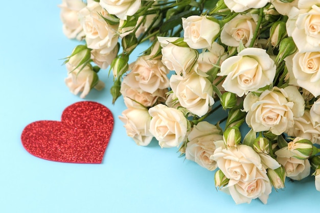 Beautiful mini roses with a red heart on a bright blue background holidays Valentine's Day closeup