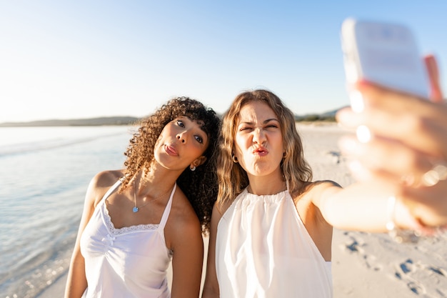 Beautiful mixed race female couple making faces doing self portrait on beach