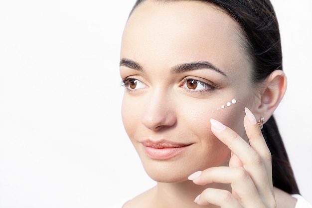 Beautiful model applying cosmetic drops of cream on her face