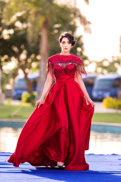 A beautiful model walks on stage during the show wearing a long red dress.