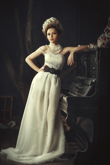 Beautiful model with a creative hairstyle wearing white lace dress is posing in a dark studio