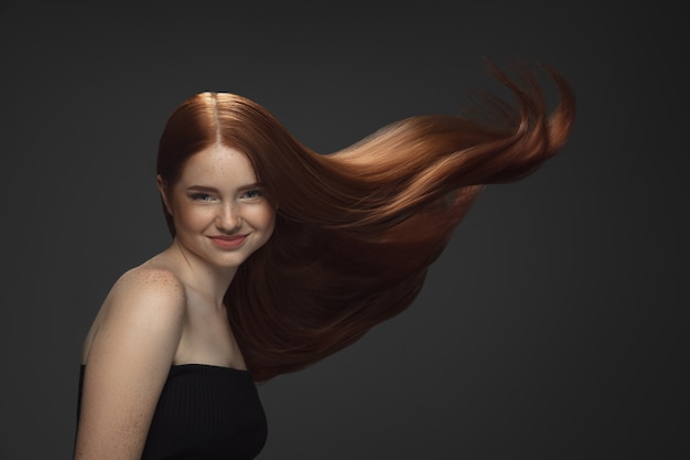 Beautiful model with long smooth flying red hair isolated on dark studio background