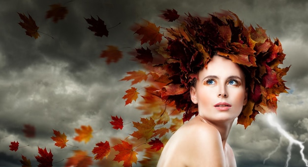 Beautiful Model Woman with Autumn Leaves. Storm Cloudy Sky, Blowing Leaves, Fashion Makeup and Perfect Beauty