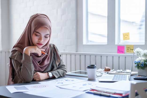 Beautiful modern Arabic business woman brown hijab discussing financial planning data in the creative workplace.