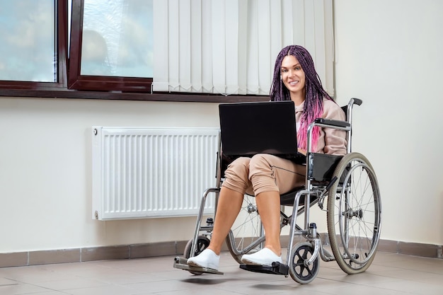 Beautiful modern disabled girl working on a laptop in a wheelchair Work from home work for the disabled freelancing remote work