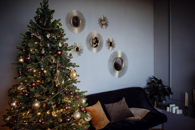 Beautiful modern gray apartment room decorated for New Year and Christmas Cute Christmas tree in a yellow garland and golden Christmas balls