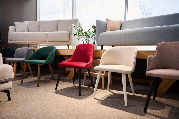 Beautiful modern retro style colorful chairs on dispay for sale in the furniture store showroom with settees couches and sofas in light pastel colors on the background