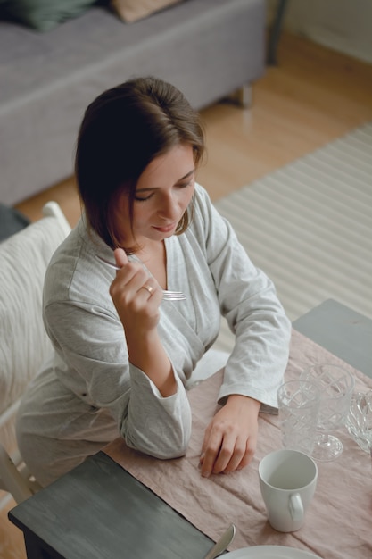 Beautiful modern woman sitting on kitchen at home. Young pretty smiling woman happily looking aside while spending time in beautiful cozy kitchen at home