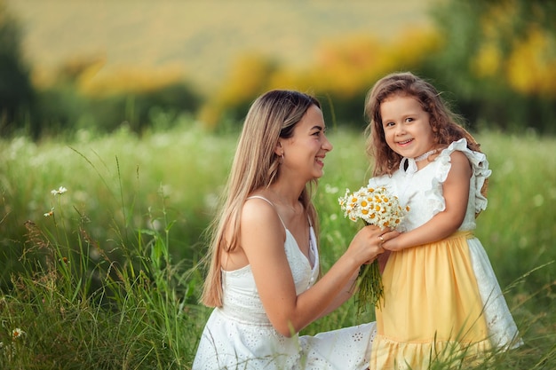 Beautiful mom Her little daughter in white dresses have fun on a walk in summer