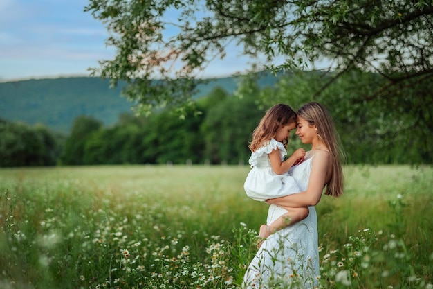 Beautiful mom Her little daughter in white dresses have fun on a walk in summer