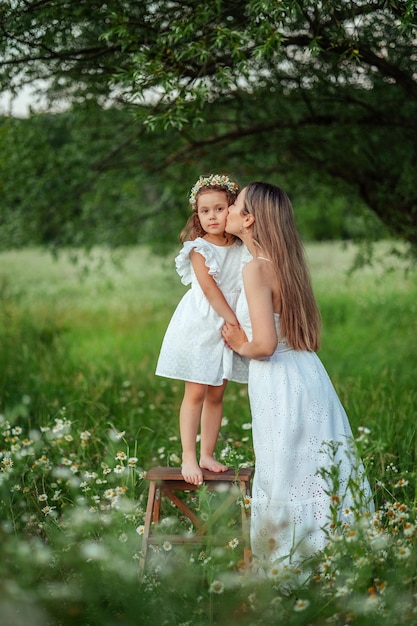 Beautiful mom Her little daughter in white dresses have fun on a walk in summer