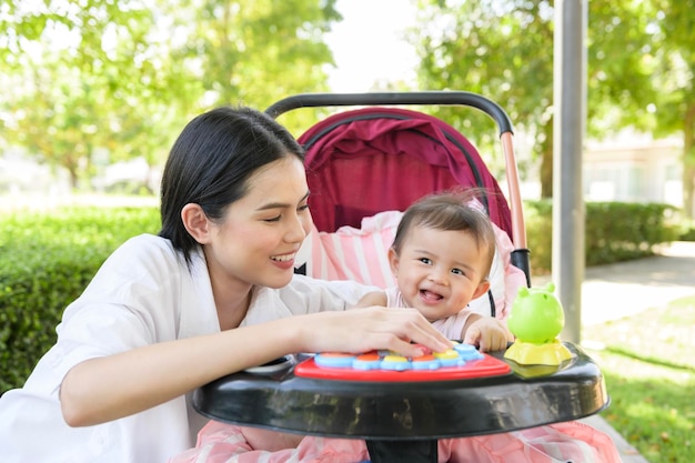 Beautiful mom with a baby girl sitting on baby trolley outdoor in sunshine day