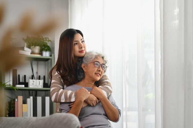 Beautiful moment of loving grown up daughter hugging mature mother from back