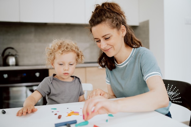 A beautiful mommy sits at the kitchen table with her preschoolaged daughter and makes something