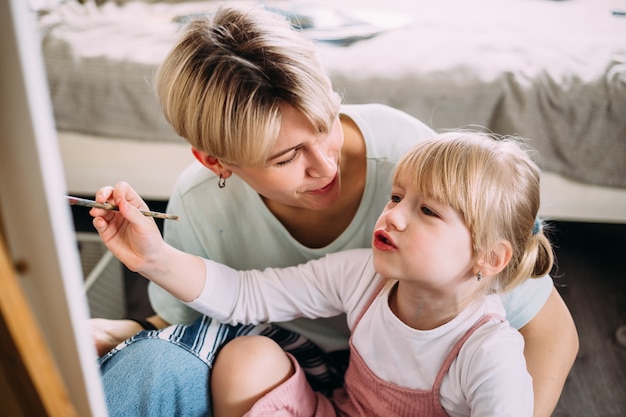 Beautiful mother artist and her child paint picture at home with acrylic paints