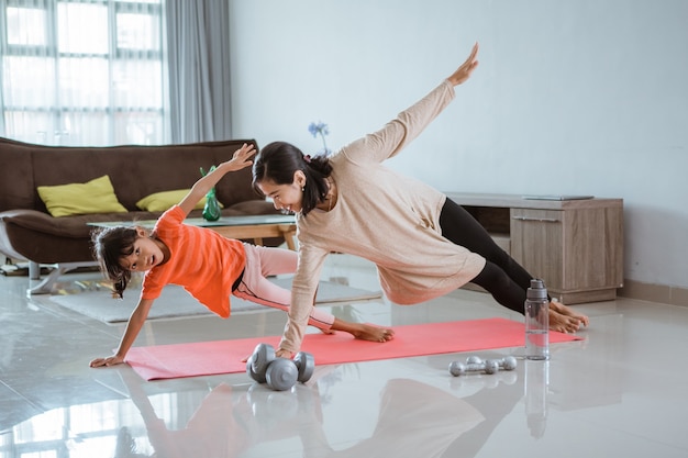 Beautiful mother and daughter doing sport exercise at at home with her daughter together