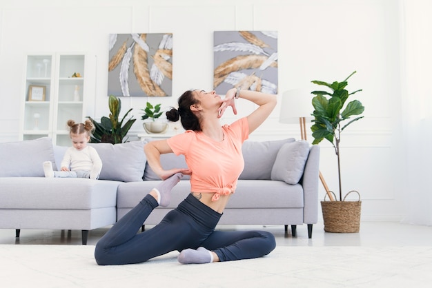 Beautiful mother doing morning stretching exercises while her daughter plays