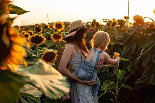 Beautiful mother holds a baby son in a sunflower field. tenderness, smiles, happiness.