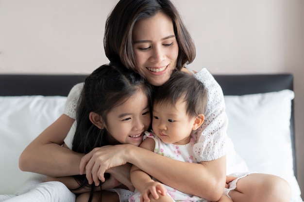 Beautiful mother hugging her children with smile sitting on bed in bedroom.