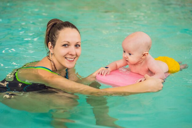 Beautiful mother teaching cute baby girl how to swim in a swimming pool Child having fun in water with mom