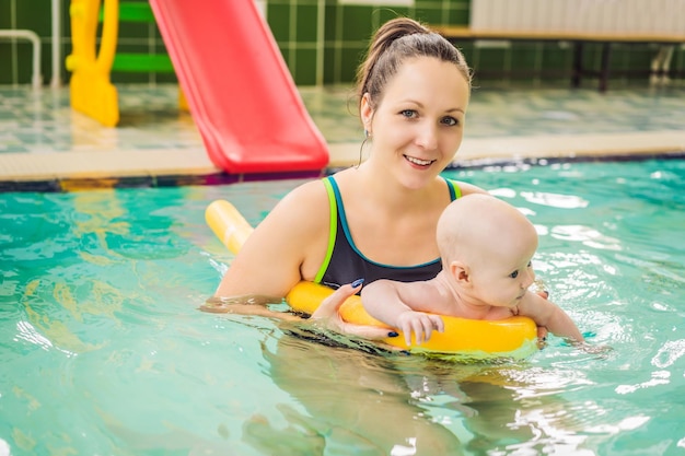 Beautiful mother teaching cute baby girl how to swim in a swimming pool Child having fun in water with mom