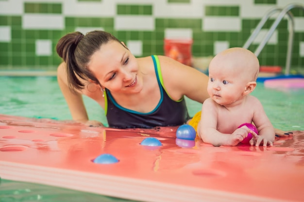 Beautiful mother teaching cute baby girl how to swim in a swimming pool Child having fun in water with mom