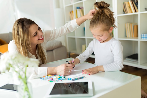 Beautiful mother with her daughter drawing with crayons at home.