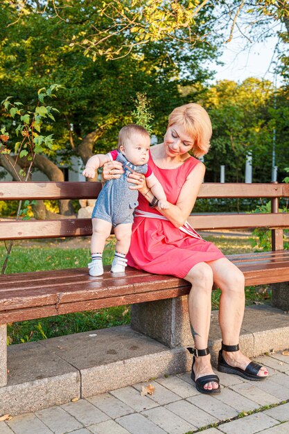 beautiful mother with her daughter and son are sitting on a bench in the park in the summer closeup