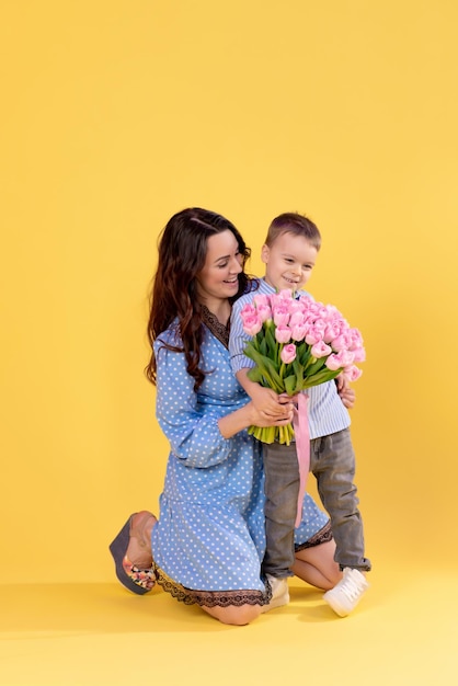 Beautiful mother with a little boy on a yellow background Loving caring mother plays with her preschool son A boy with a big bouquet of flowers child development