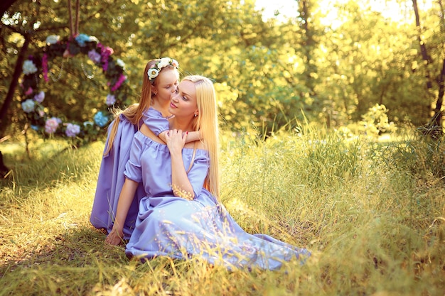 Beautiful mother with long blonde hair posing and playing with her daughter in similar lavender dresses in the park outdoor