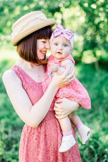 Beautiful Mother with the straw hat And her little daughter outdoors family look in in a pink dress . Outdoor Portrait of happy family. family look. mom kisses daughter in a cheek.