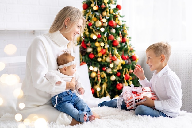 beautiful mother with two children give New Years gifts at home under the tree celebrate Christmas