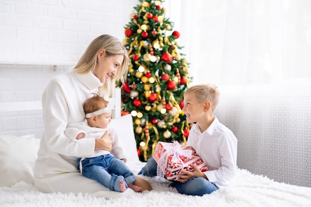 beautiful mother with two children give New Years gifts at home under the tree celebrate Christmas