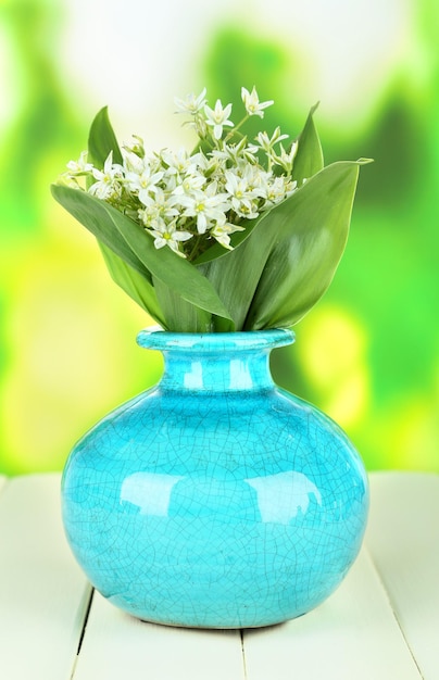 Beautiful mountain daffodils in color vase on wooden table on bright background