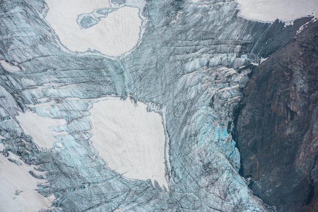 Beautiful mountain landscape with vertical glacier tongue with cracks among rocks Awesome natural backdrop of large glacier with icefall Nature texture of mountain glacier with fissures close up