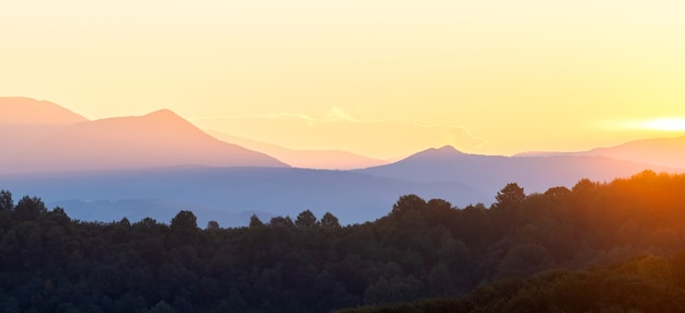 Beautiful mountain panorama of landscape with hazy peaks and foggy wooded valley at sunset.