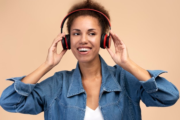 Beautiful multiethnic woman with afro hairstyle singing song wearing headphones beige background