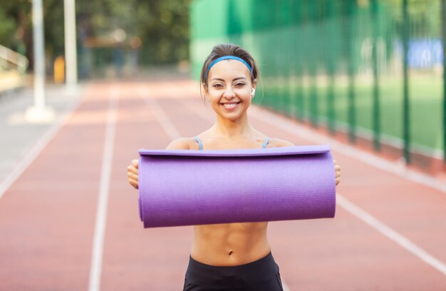 Beautiful muscular woman with exercise mat in stadium