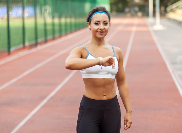 Beautiful muscular woman with perfect body and smart bracelet on stadium Heart rate monitoring