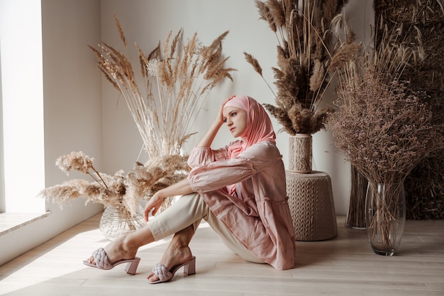 Beautiful muslim arabian woman wearing pink hijab sitting on floor and smiling