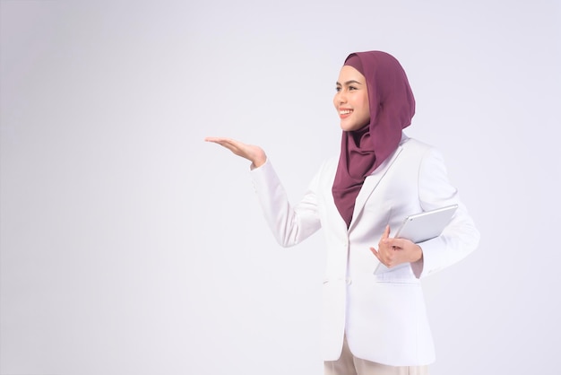 Beautiful muslim business woman wearing white suit with hijab holding tablet in studiox9