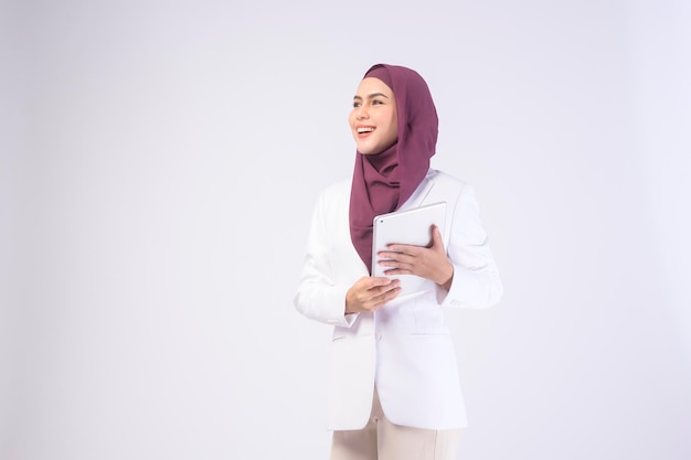 Beautiful muslim business woman wearing white suit with hijab holding tablet in studiox9