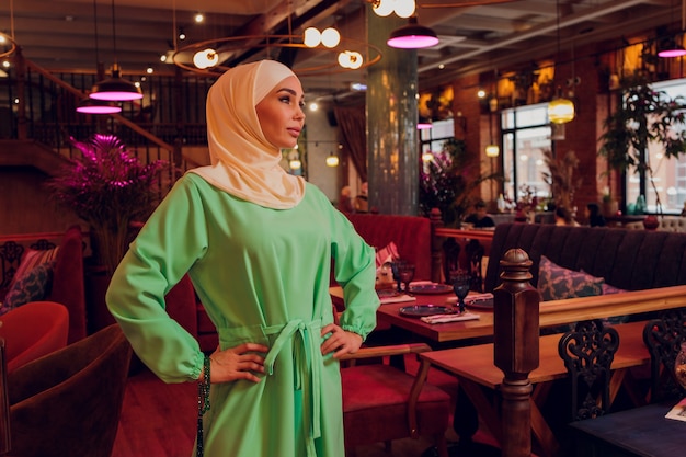 Beautiful Muslim girl in hijab smiling, waiting for her food in a restaurant.