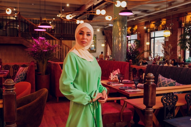 Beautiful Muslim girl in hijab smiling, waiting for her food in a restaurant.