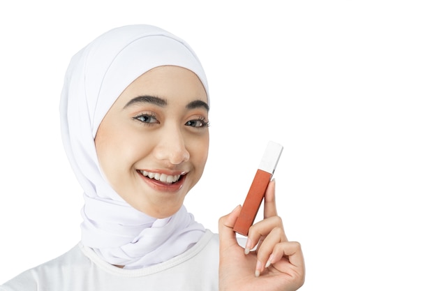 Beautiful muslim woman in hijab smiling while holding lipstick bottle