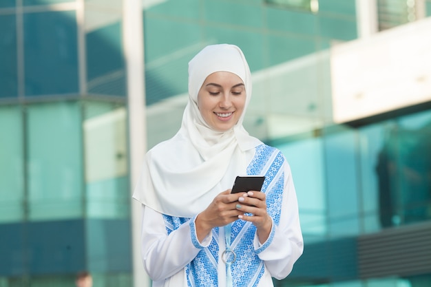 Beautiful muslim woman texting on a mobile phone outdoors.