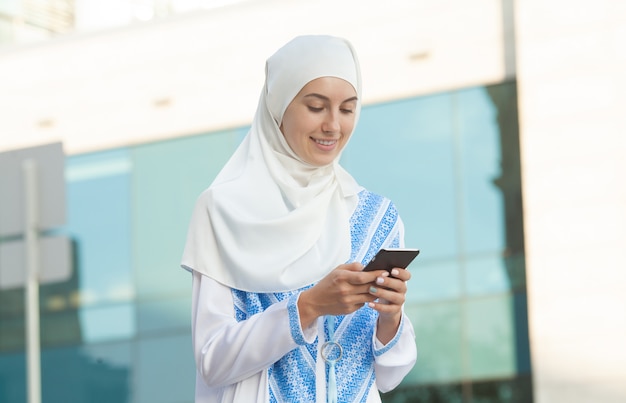 Beautiful muslim woman texting on a mobile phone outdoors.