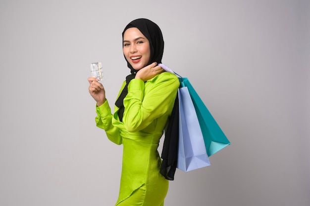 Beautiful musllim woman with hijab holding credit card and shopping bag over white background