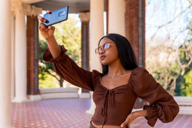 A beautiful natural young African woman in a park Smiling with sunglasses taking a selfie