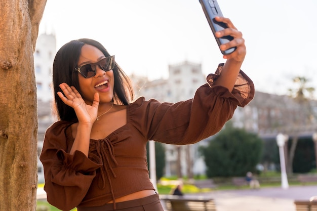 A beautiful natural young African woman in a park With sunglasses doing a live on social networks for followers